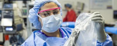 An OR nurse in a mask and scrubs applies a covering to a robotic surgery device.